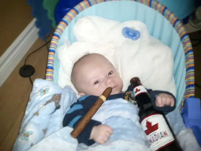 Baby holding a cigar and beer bottle in baby carrier