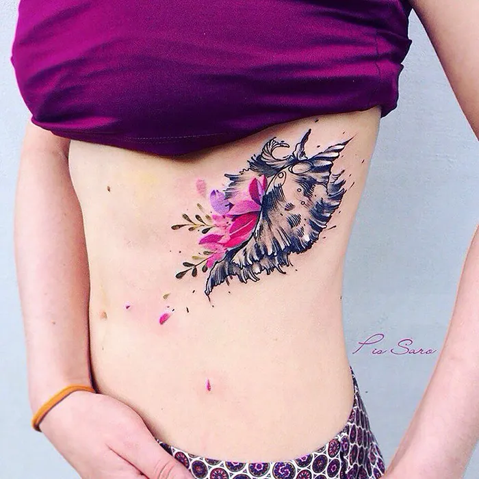Ethereal nature tattoo of a floral and feather design on a person's side, inspired by the changing seasons.