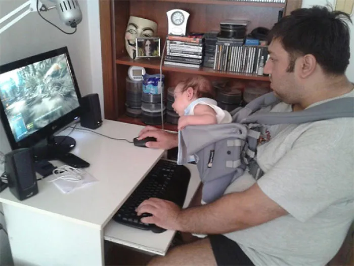 Dad playing computer games with baby in front carrier reasons kids can't be left alone with dads