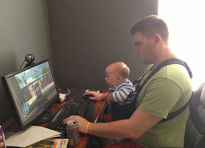 Dad playing computer game with baby strapped in front