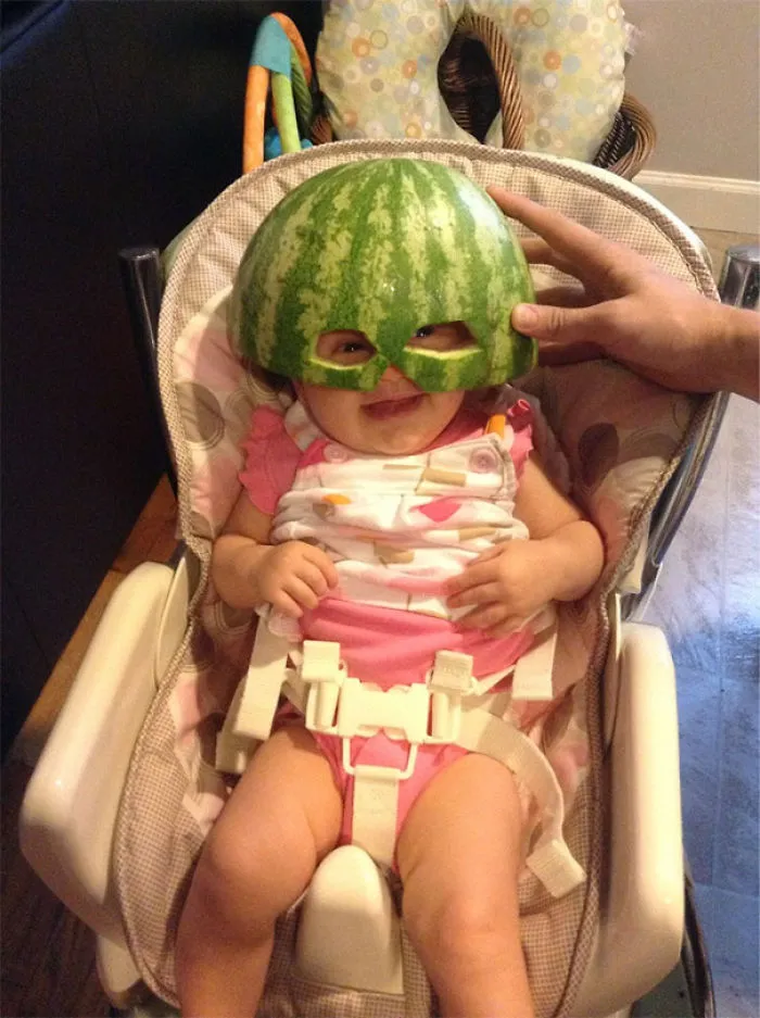 Baby wearing watermelon helmet while seated in high chair