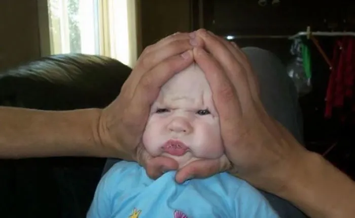 Hands squishing baby face humorously demonstrating kids left alone with dads