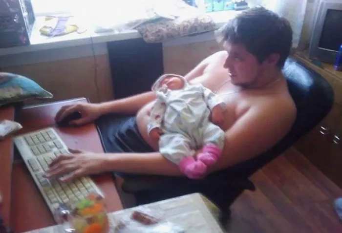 Young dad working on computer holding baby in arms highlighting kids left alone with dads
