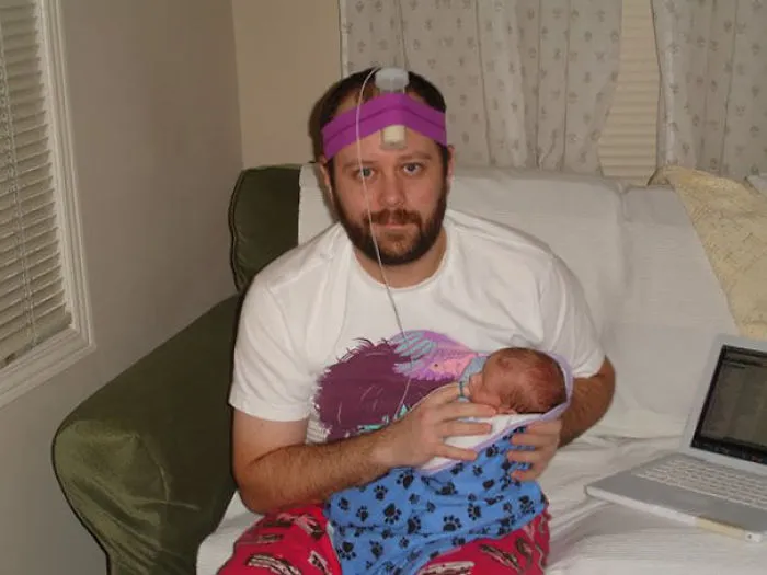 Man holding newborn baby with strange gadget on head representing kids left alone with dads