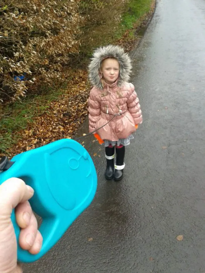 Child wearing coat walking on a leash on a path