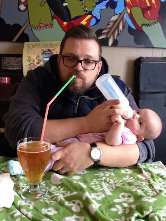 Dad multitasking drinking and feeding baby with bottle