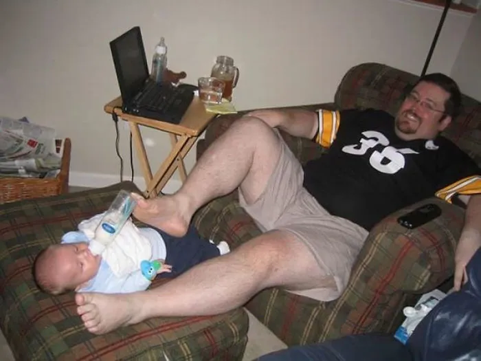 Dad using his foot to feed a baby bottle, illustrating funny parenting moments with kids