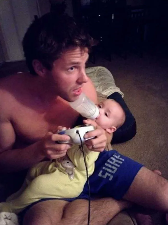 Man feeding baby with bottle while playing video games reasons kids can't be left alone with dads