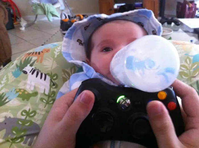 Baby fed with bottle held by hands holding video game controller reasons kids can't be left alone with dads