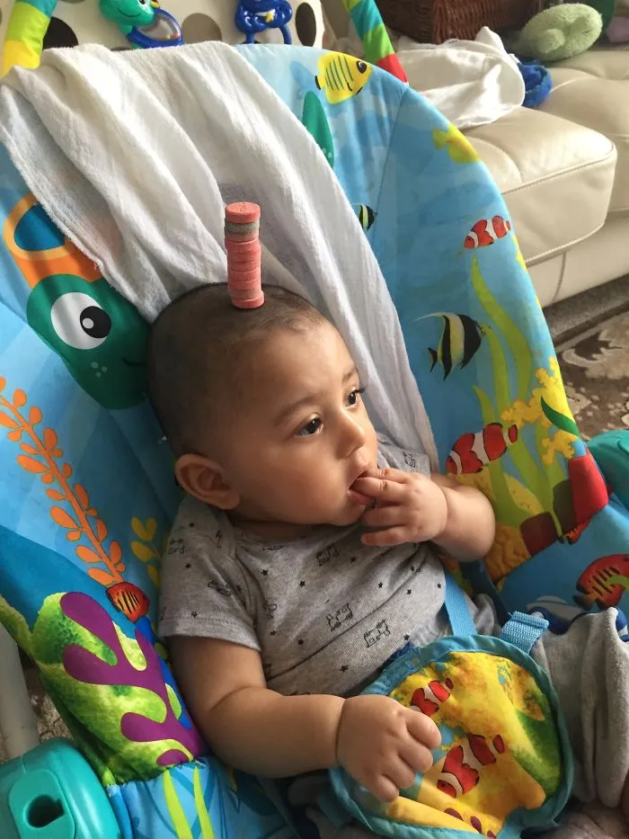 Baby with cookies stacked on head in colorful baby seat