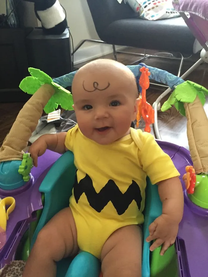 Smiling baby with a drawn swirl on forehead sitting in a baby chair kids alone with dads