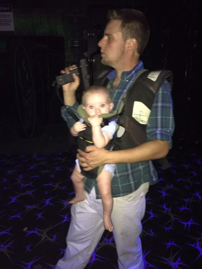 Man holding baby in a carrier in a dark room kids alone with dads