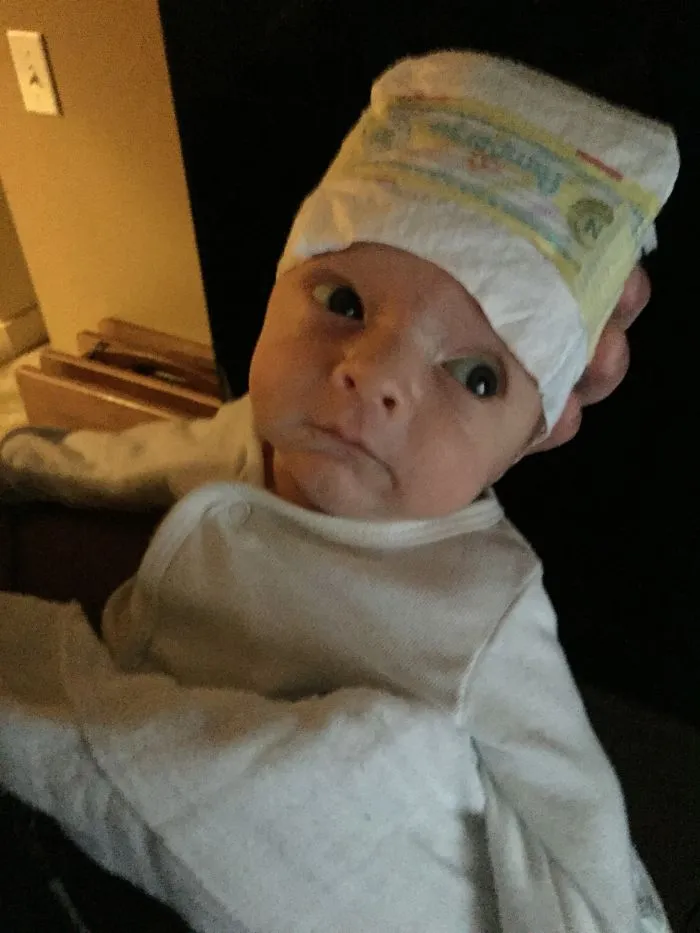 Newborn baby wearing a diaper on head illustrating kids alone with dads