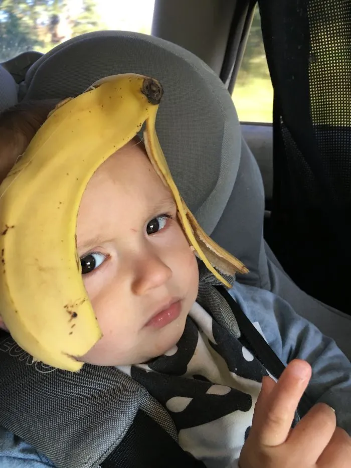 Child wearing banana peel on head sitting in car seat, funny kids can't be left alone with their dads