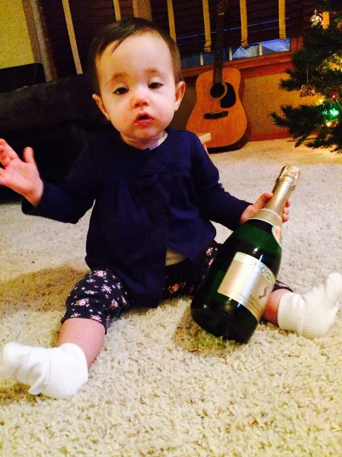 Baby holding champagne bottle near Christmas tree shows kids can't be left alone with dads