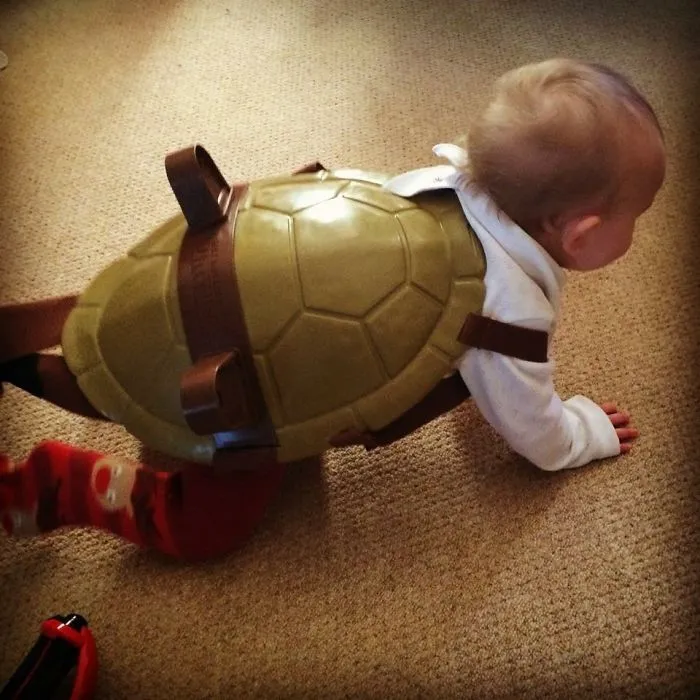Baby crawling in turtle shell costume exemplifying kids can't be left alone with dads