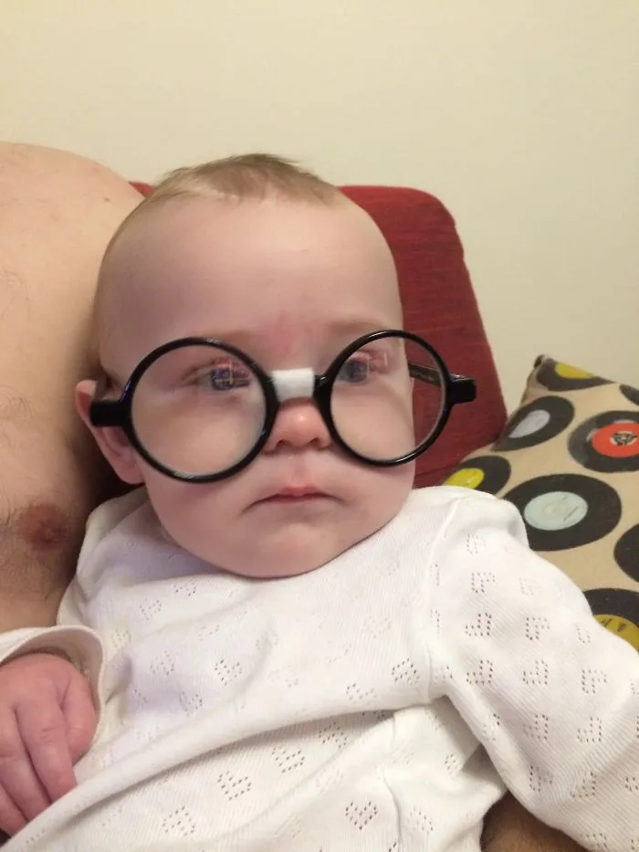 Baby in large glasses looking serious for kids can't be left alone with dads