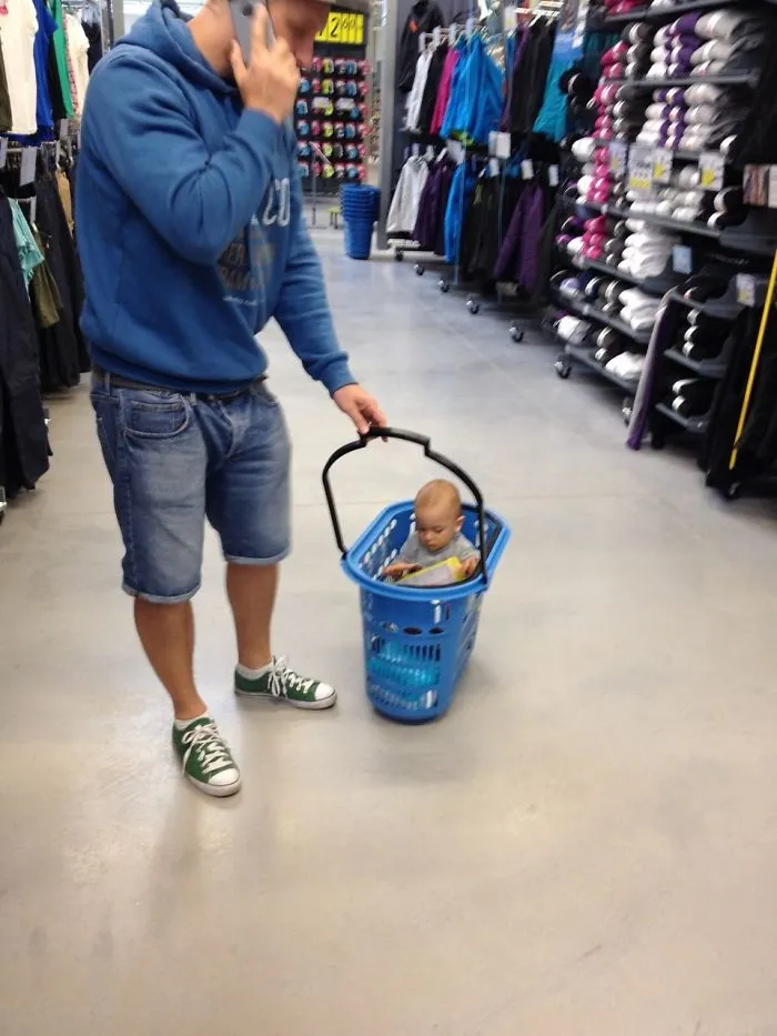 Father pulling baby seated inside blue laundry basket in store