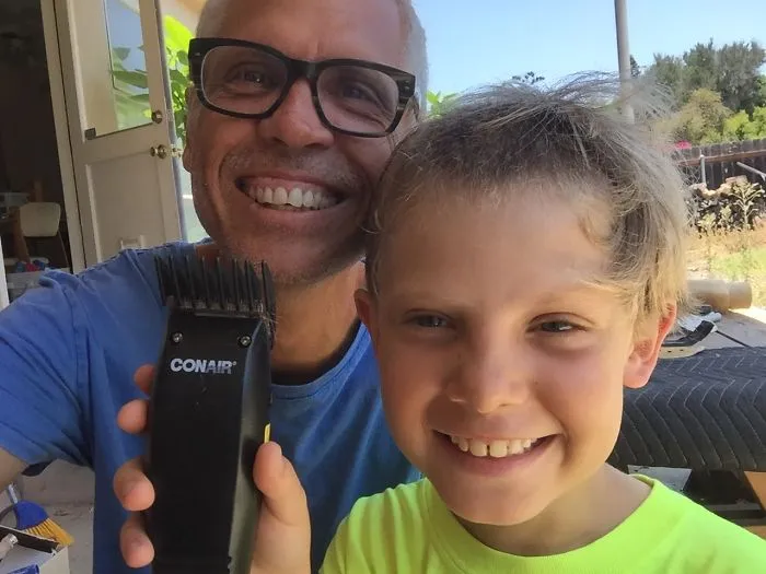 Smiling dad holding hair clippers next to happy child