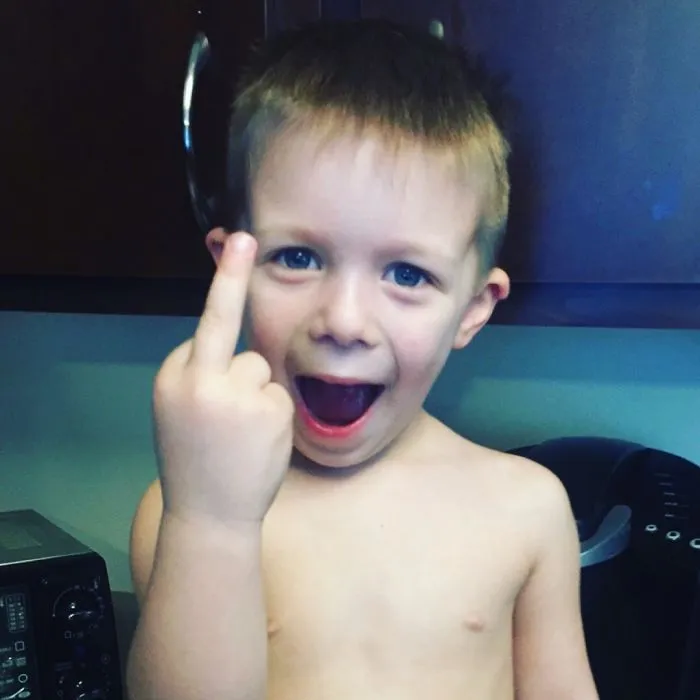 Young boy making rude gesture at home