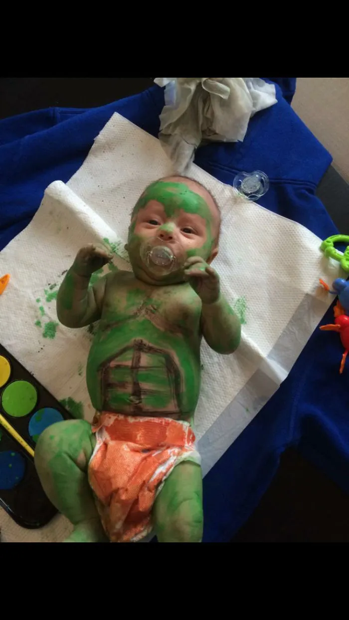Baby covered in green paint with pacifier in messy playtime