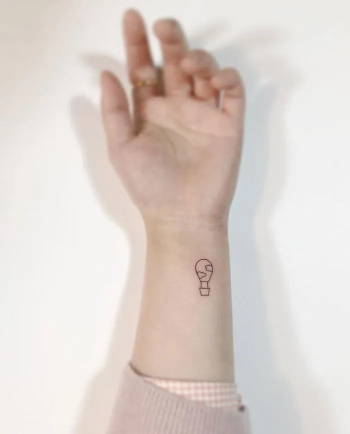 Minimalist tattoo of a small light bulb on a person's wrist, created by a Korean artist.