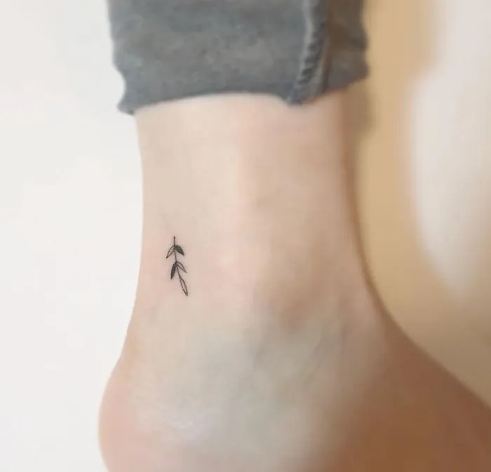Minimalist tattoo featuring delicate leaf design on ankle by Korean artist.
