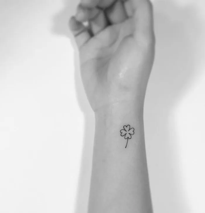 Minimalist tattoo of a small four-leaf clover on a wrist, designed by a Korean artist.