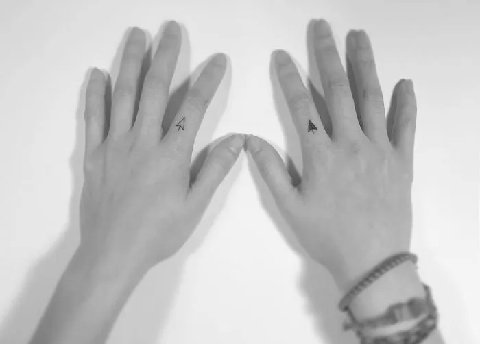 Minimalist tattoos on hands by Korean artist, featuring small arrow designs on fingers.