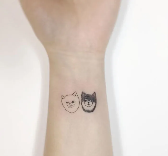 Minimalist tattoos of two cute animal faces on a person's wrist by a Korean artist.