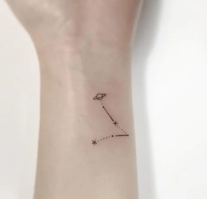 Minimalist tattoo of a constellation and planet on an inner wrist, designed by a Korean artist.