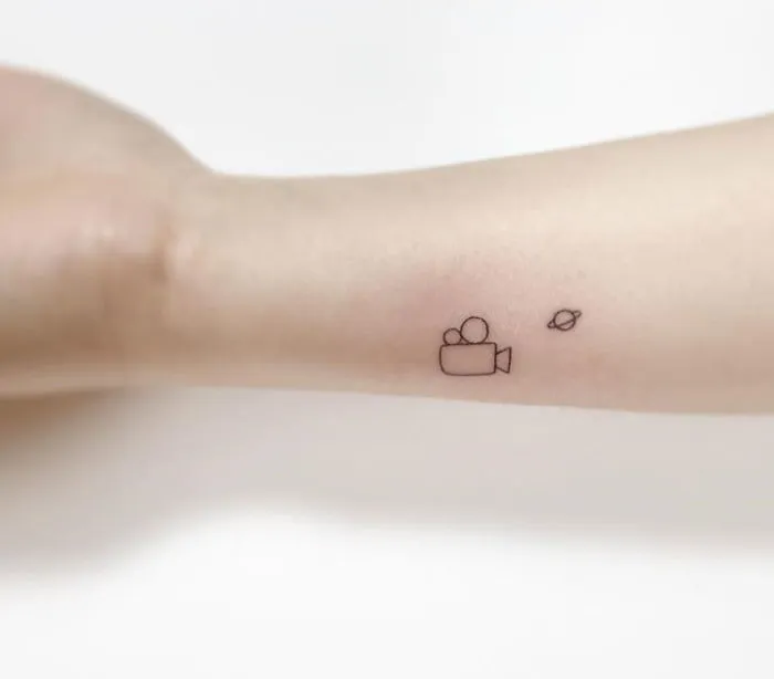 Minimalist tattoos of a camera and planet inked on forearm by Korean artist.