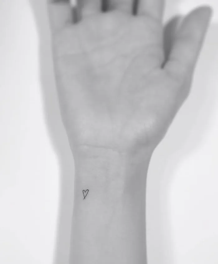 Minimalist tattoo of a small heart on a person's wrist, designed by a Korean artist.