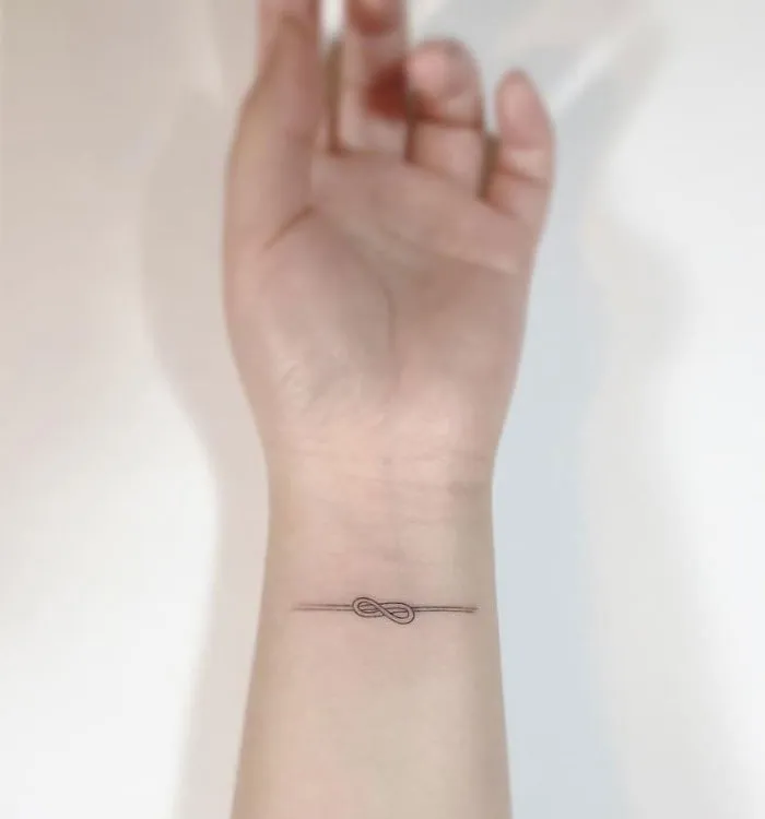 Minimalist tattoo on a wrist with a small infinity design by a Korean artist.
