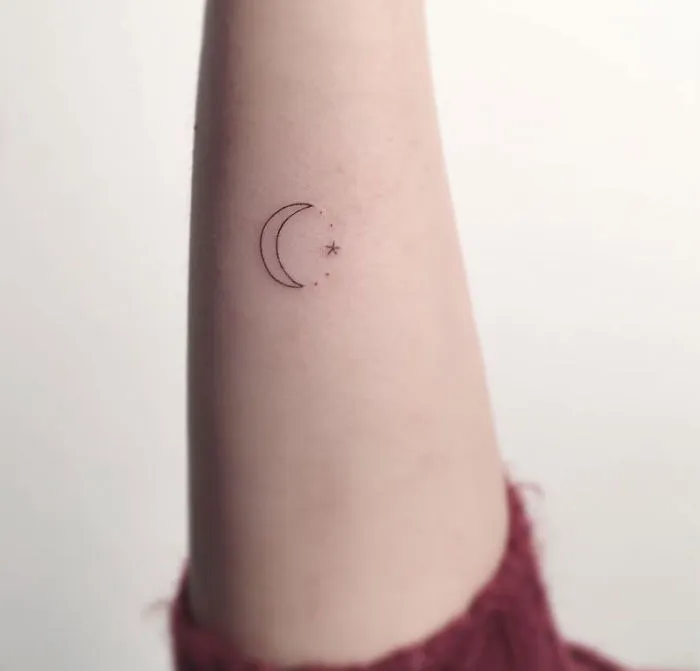 Minimalist tattoo of a crescent moon and star on an arm, created by a Korean artist.