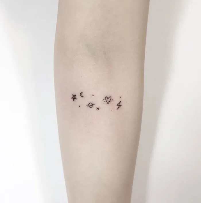 Minimalist tattoo with star, moon, planet, heart, and lightning symbols on a forearm by a Korean artist.