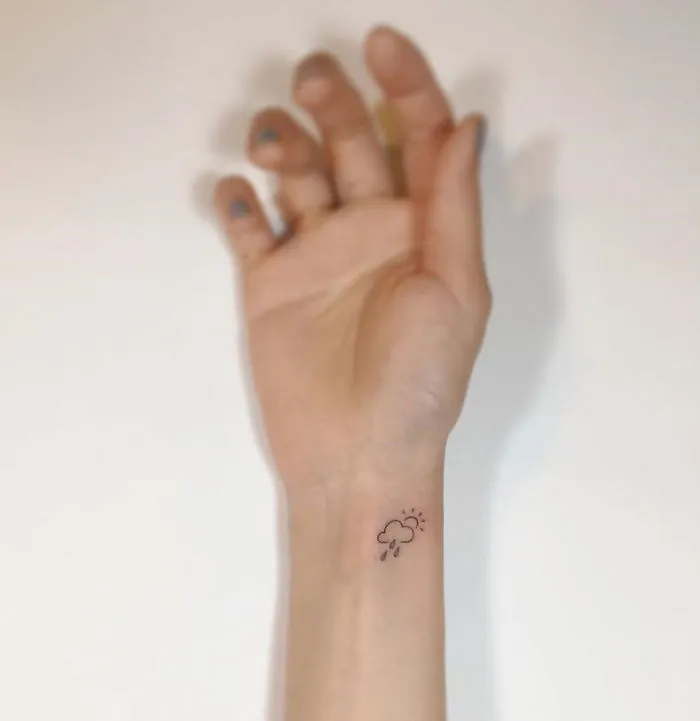 Minimalist tattoo of a cloud with rain and sun on a wrist by Korean artist.