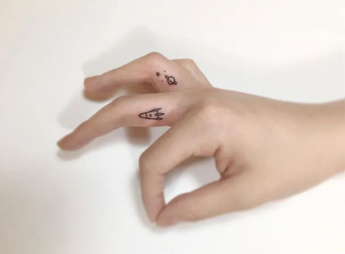 Minimalist tattoos of a rocket and planets on fingers by a Korean artist.