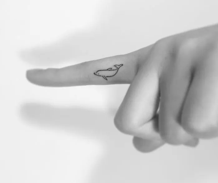 Minimalist tattoo of a whale on a finger, created by a Korean artist.