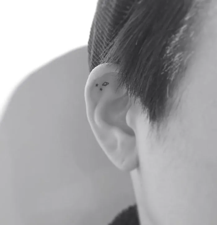 Minimalist tattoo of stars and an infinity symbol on the inner ear, designed by a Korean artist.