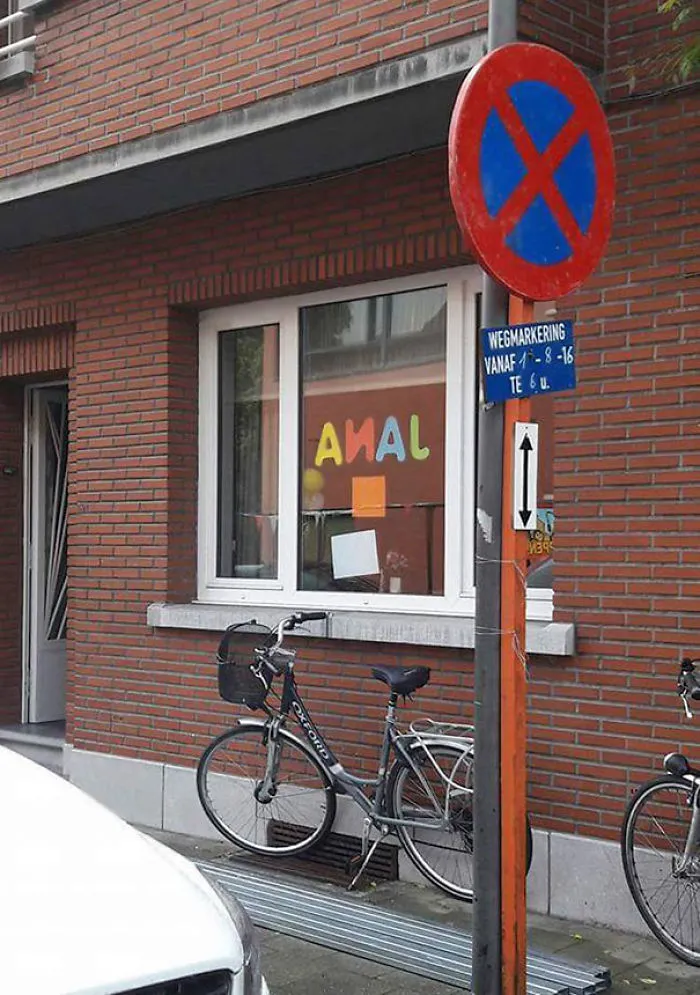 Sign fail with jumbled window letters, bike leaning against a brick wall, and a no parking sign.