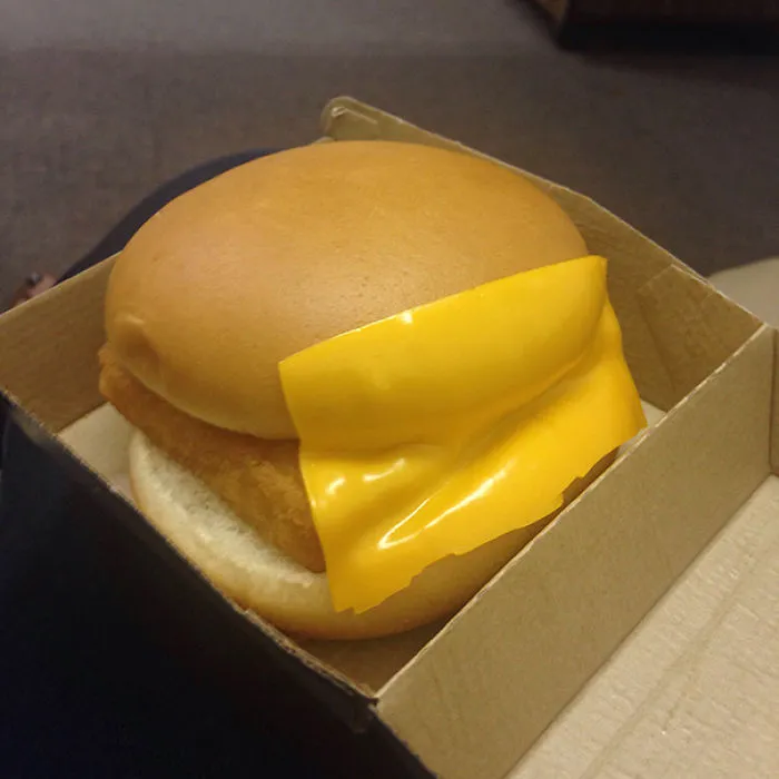 Burger with cheese slice misplaced halfway outside the bun; a humorous example of job failure.