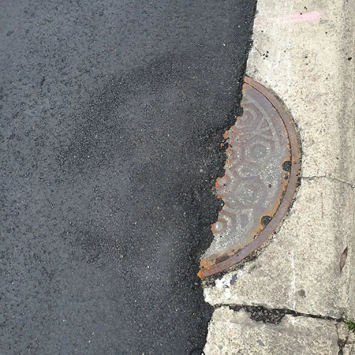 Manhole cover misaligned after road paving, illustrating job failure.