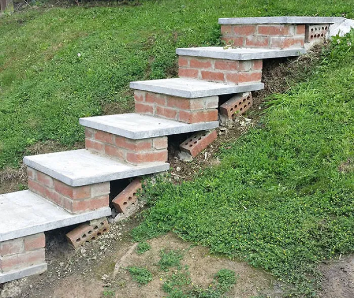 Uneven brick stairs in grassy hillside, showcasing construction fail.
