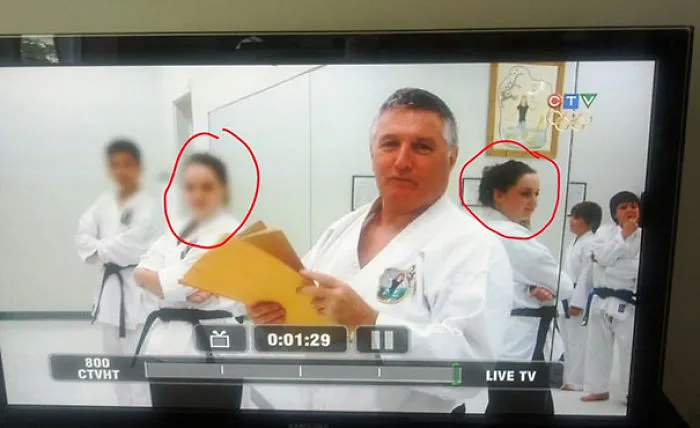 Karate instructor holding papers, with two students blurred on TV, highlighting a job fail in live broadcast.