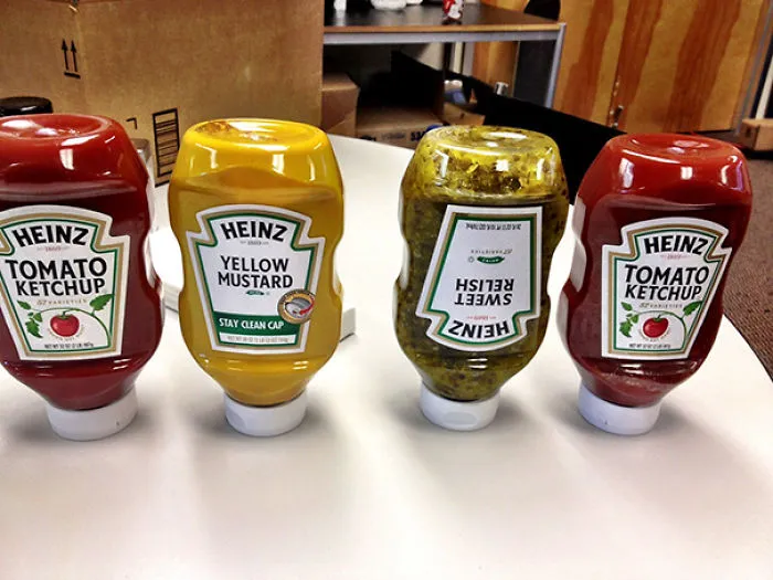 Condiment bottles on a table with one upside down, showcasing product alignment failure.