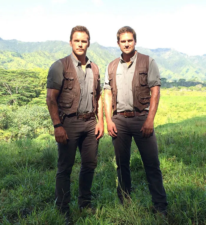 Two men dressed alike in outdoor adventure gear standing in a grassy field illustrating Hollywood body doubles concept.