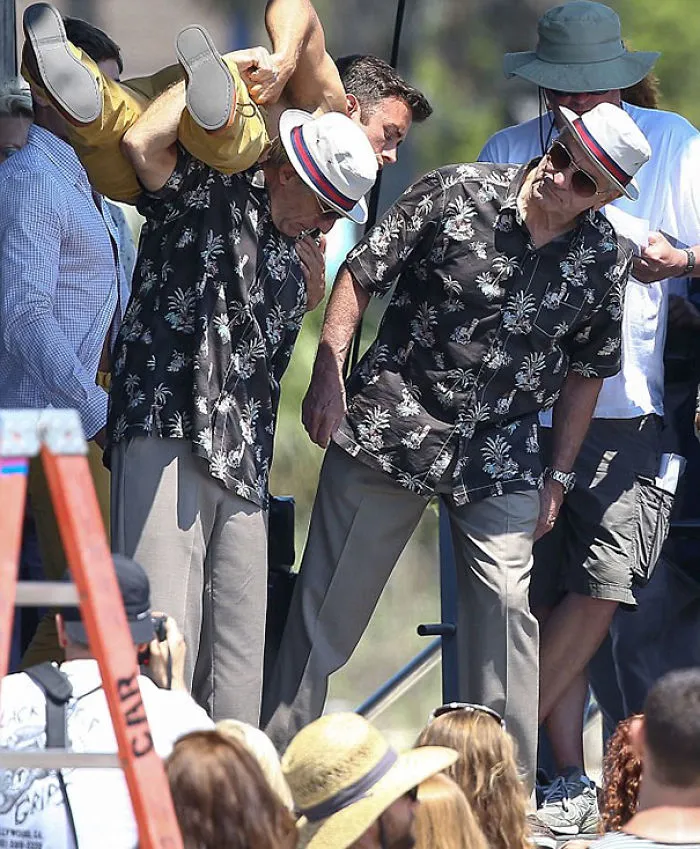 Two men in matching floral shirts and hats revealing body doubles during a Hollywood celebrity film shoot.