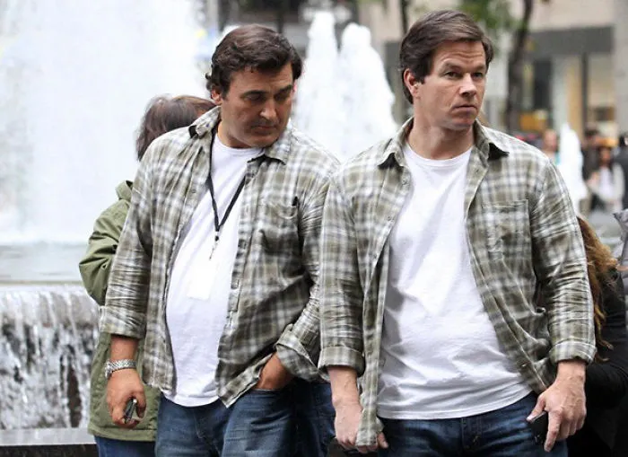 Two men in matching plaid shirts and white tees walking near a fountain, showcasing Hollywood celebrity body doubles.