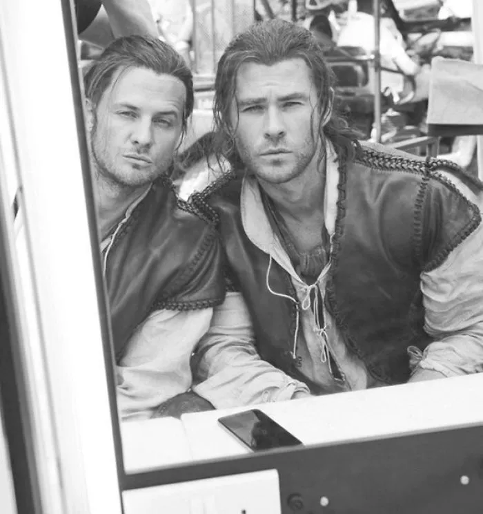 Two men in period costumes, one likely a celebrity’s body double, sitting and looking into a mirror on set.